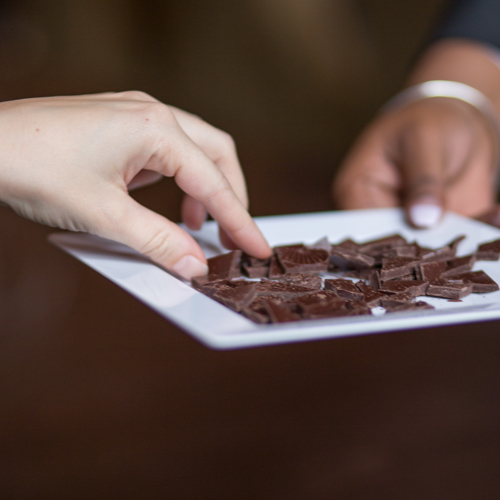 Close up van hand die stukje chocolade van wit bordje pakt.