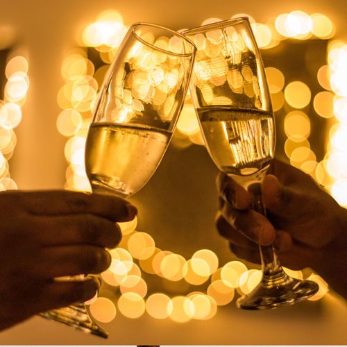 Close up van 2 handen die proosten met champagneglazen met kerstverlichting op achtergrond